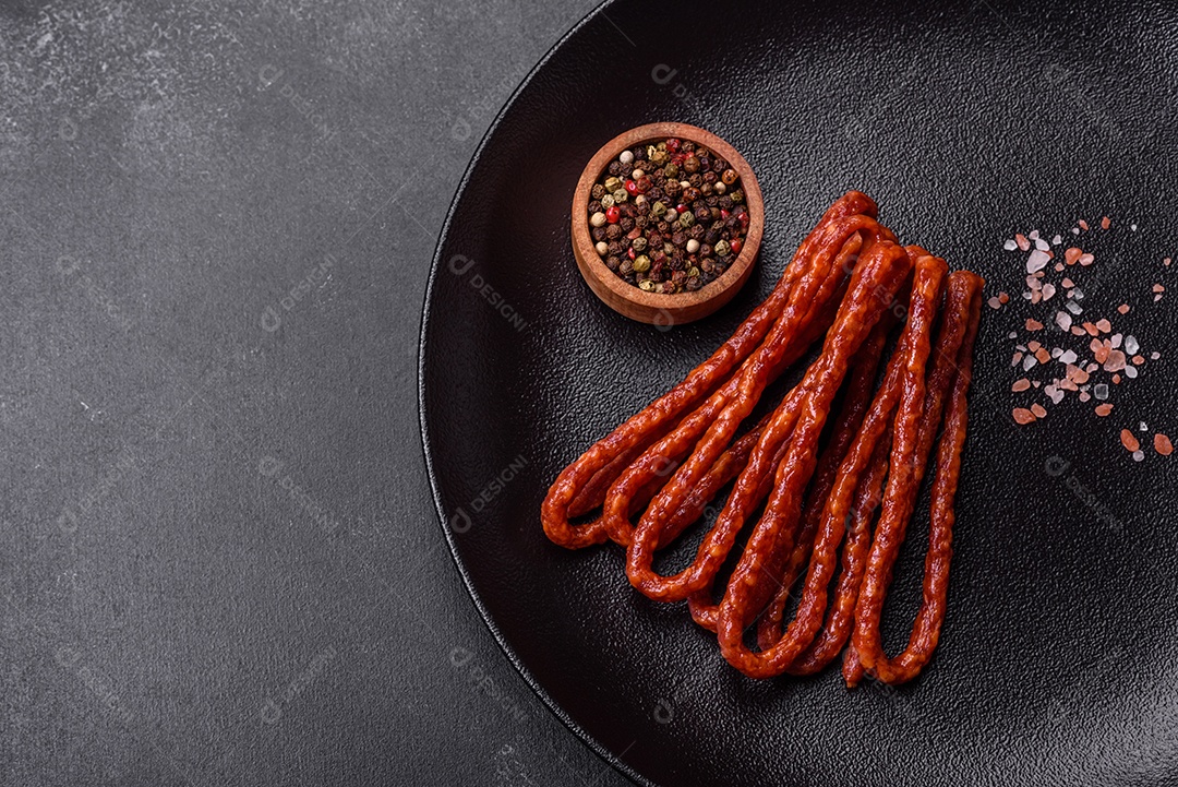 Deliciosas salsichas finas de carne fumada com especiarias e ervas sobre um fundo escuro de concreto