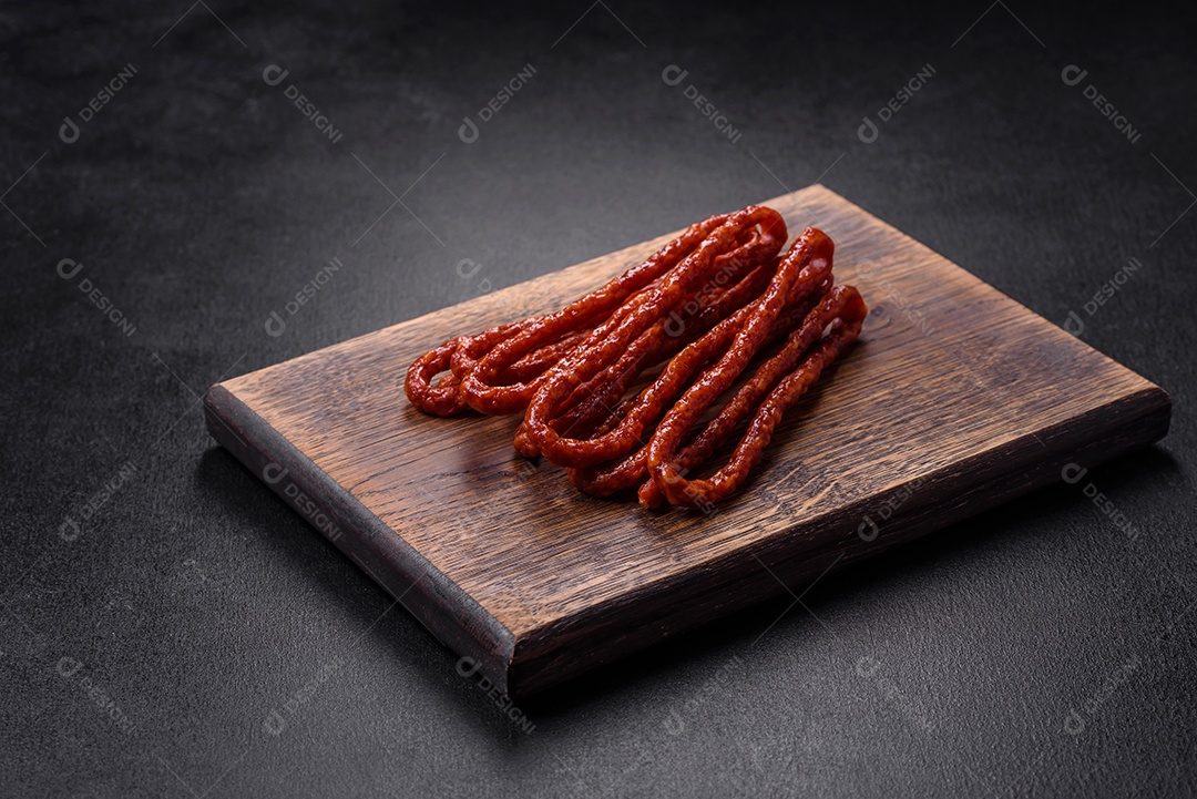 Deliciosas salsichas finas de carne fumada com especiarias e ervas sobre um fundo escuro de concreto