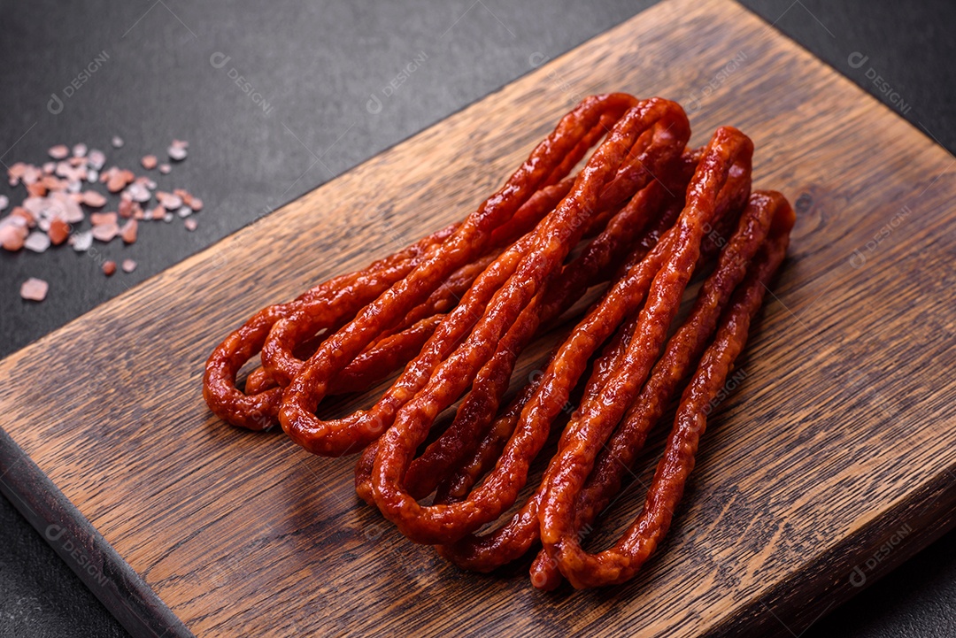 Deliciosas salsichas finas de carne fumada com especiarias e ervas sobre um fundo escuro de concreto