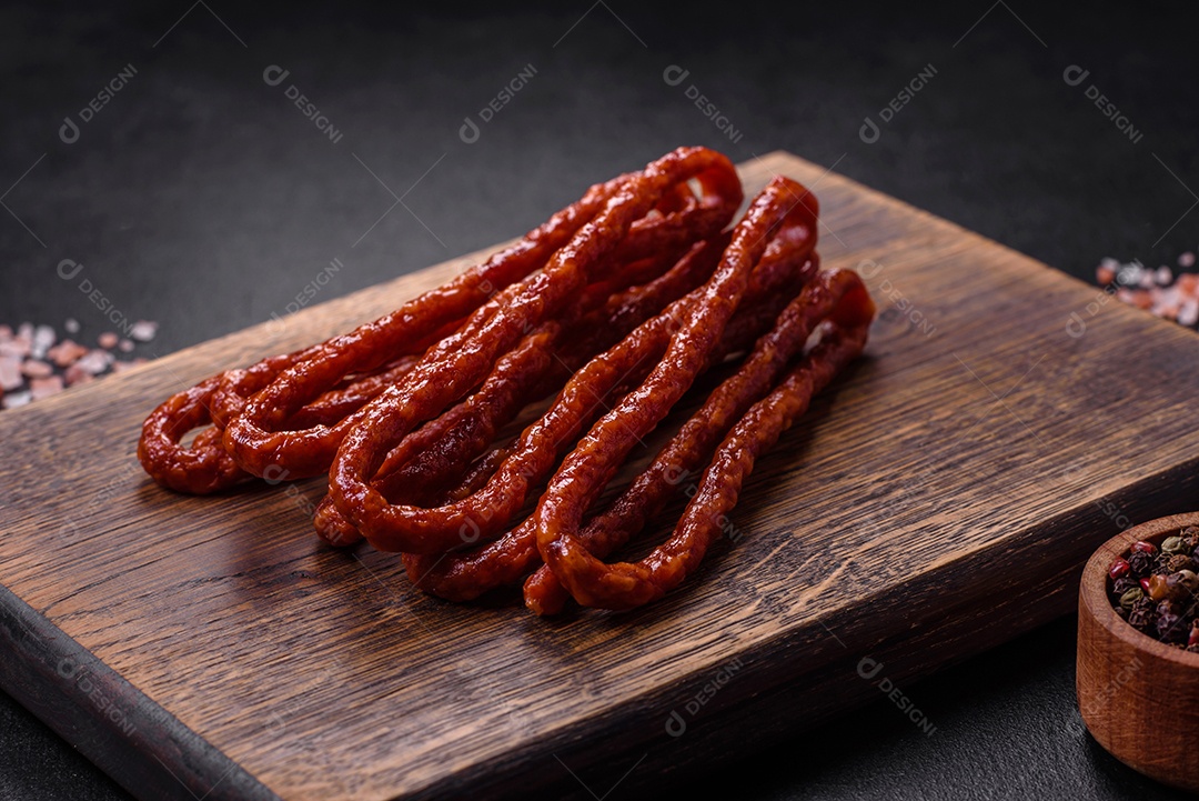 Deliciosas salsichas finas de carne fumada com especiarias e ervas sobre um fundo escuro de concreto