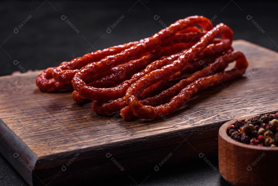 Deliciosas salsichas finas de carne fumada com especiarias e ervas sobre um fundo escuro de concreto