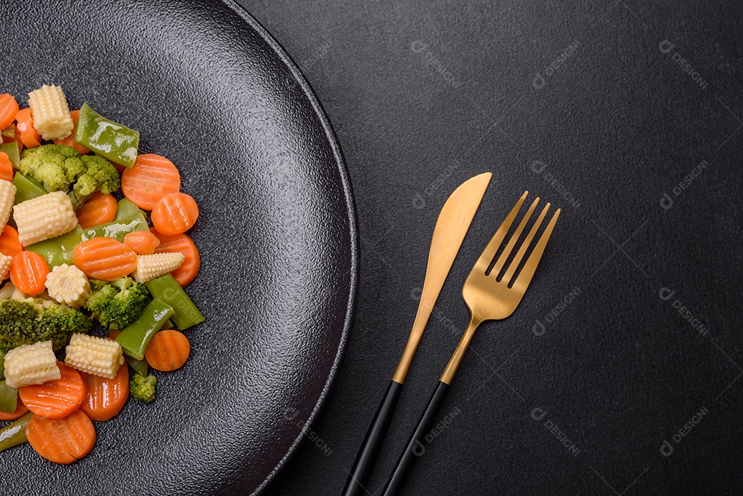 Uma mistura de vegetais: cenouras, pequenas espigas de milho, grãos de aspargos cozidos no vapor em um prato de cerâmica preta