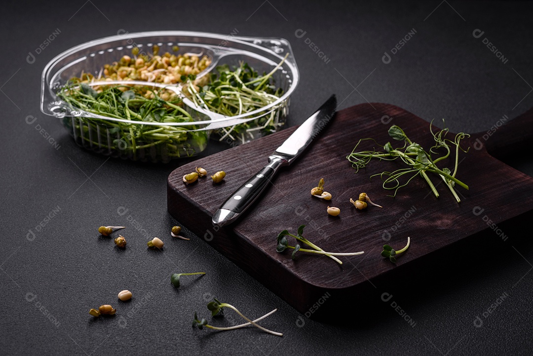 Um conjunto ou mistura de microgreens de ervilha, mostarda e feijão mungo germinado em uma caixa de plástico repartida sobre um fundo escuro de concreto