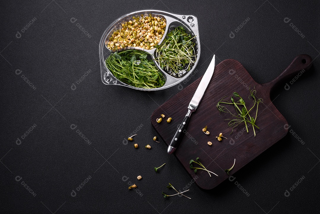Um conjunto ou mistura de microgreens de ervilha, mostarda e feijão mungo germinado em uma caixa de plástico repartida sobre um fundo escuro de concreto