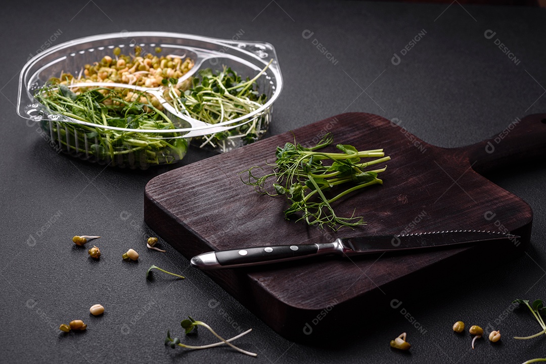 Um conjunto ou mistura de microgreens de ervilha, mostarda e feijão mungo germinado em uma caixa de plástico repartida sobre um fundo escuro de concreto