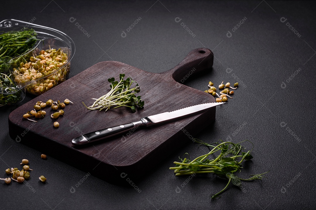 Um conjunto ou mistura de microgreens de ervilha, mostarda e feijão mungo germinado em uma caixa de plástico repartida sobre um fundo escuro de concreto