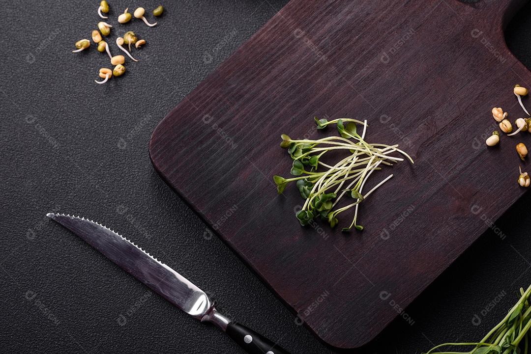 Um conjunto ou mistura de microgreens de ervilha, mostarda e feijão mungo germinado em uma caixa de plástico repartida sobre um fundo escuro de concreto