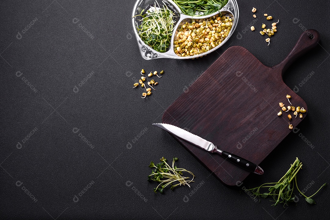 Um conjunto ou mistura de microgreens de ervilha, mostarda e feijão mungo germinado em uma caixa de plástico repartida sobre um fundo escuro de concreto