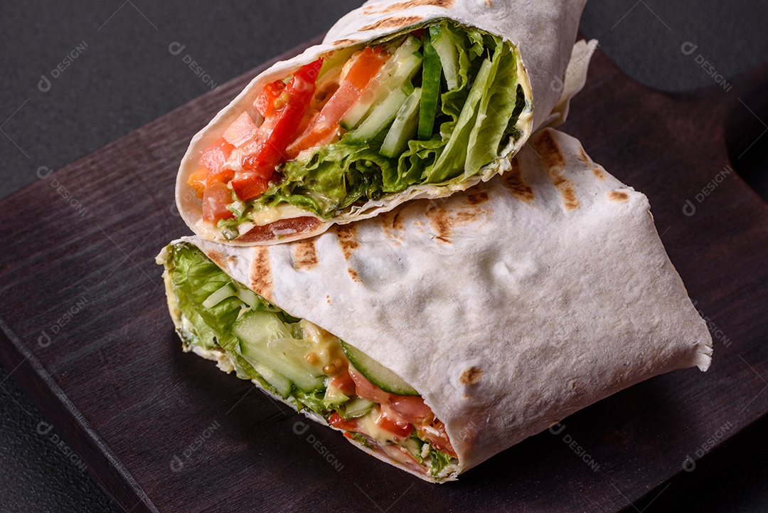 Delicioso shawarma fresco com tomate, pimentão, pepino e molhos em um fundo escuro de concreto. Comida rápida