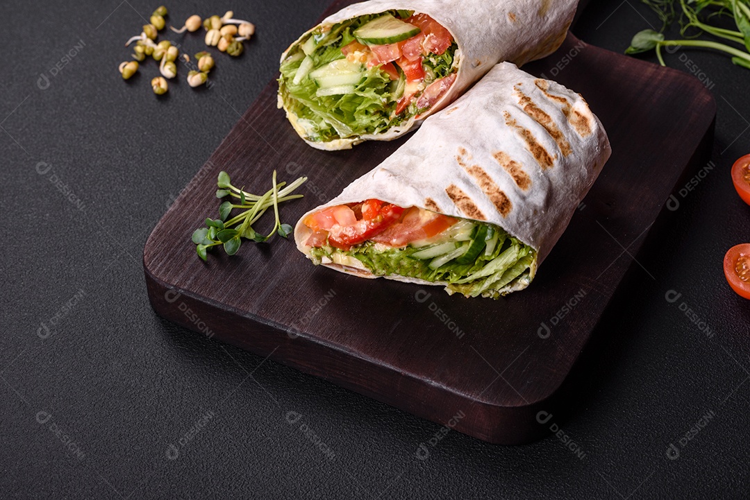 Delicioso shawarma fresco com tomate, pimentão, pepino e molhos em um fundo escuro de concreto. Comida rápida