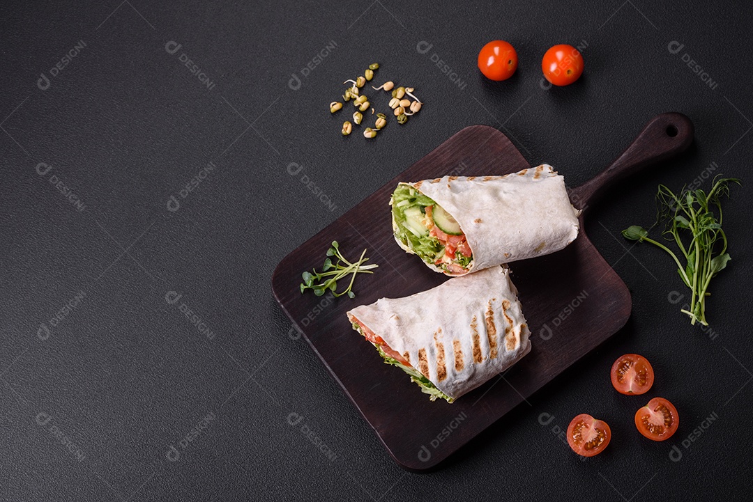 Delicioso shawarma fresco com tomate, pimentão, pepino e molhos em um fundo escuro de concreto. Comida rápida