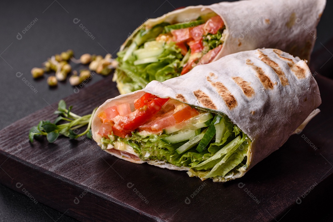 Delicioso shawarma fresco com tomate, pimentão, pepino e molhos em um fundo escuro de concreto. Comida rápida