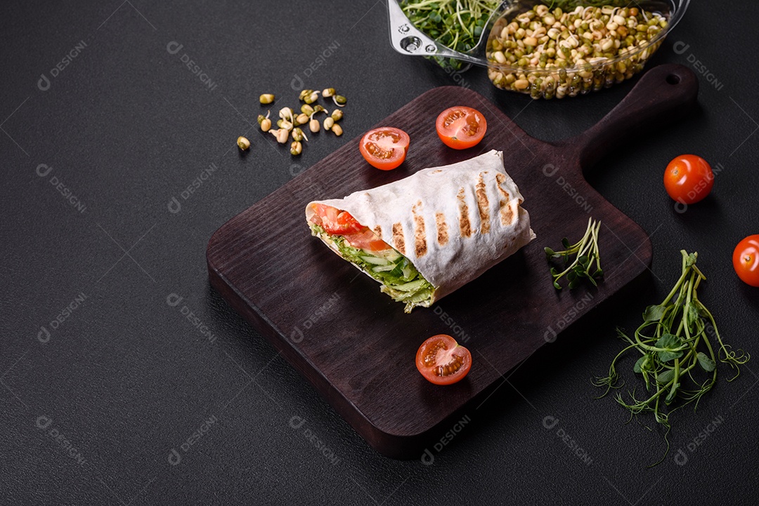 Delicioso shawarma fresco com tomate, pimentão, pepino e molhos em um fundo escuro de concreto. Comida rápida