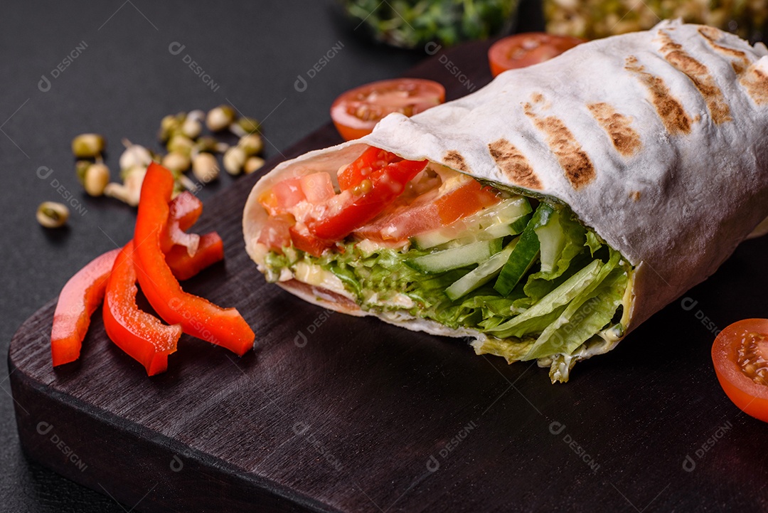 Delicioso shawarma fresco com tomate, pimentão, pepino e molhos em um fundo escuro de concreto. Comida rápida