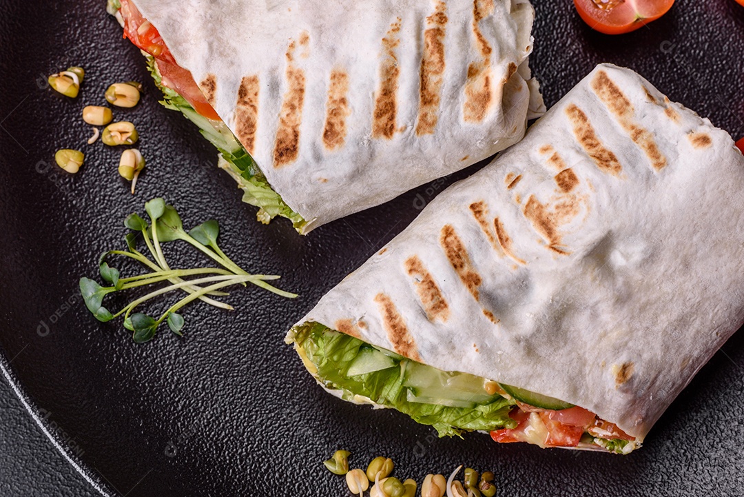 Delicioso shawarma fresco com tomate, pimentão, pepino e molhos em um fundo escuro de concreto. Comida rápida