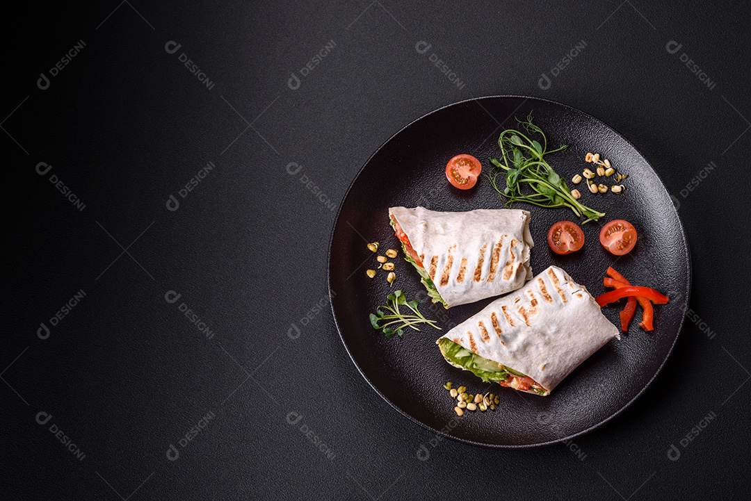 Delicioso shawarma fresco com tomate, pimentão, pepino e molhos em um fundo escuro de concreto. Comida rápida