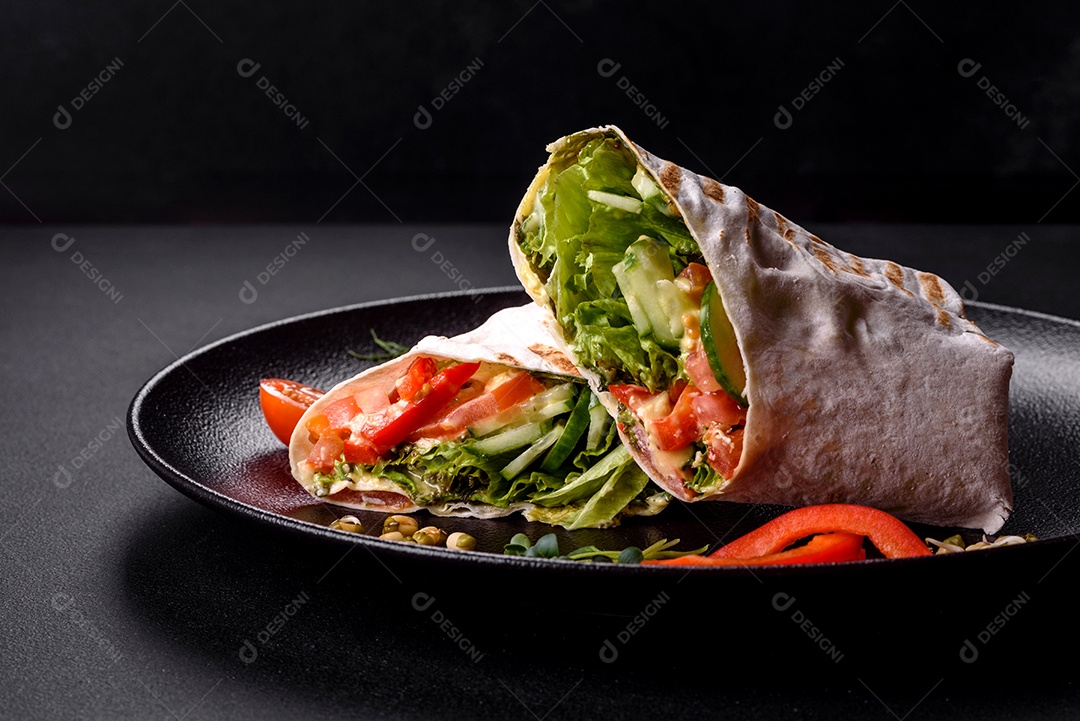 Delicioso shawarma fresco com tomate, pimentão, pepino e molhos em um fundo escuro de concreto. Comida rápida