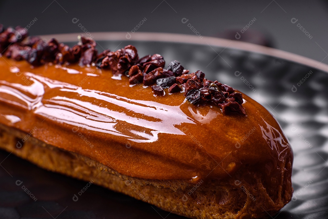 Delicioso eclair fresco com creme de chocolate em uma placa de cerâmica preta sobre um fundo escuro de concreto