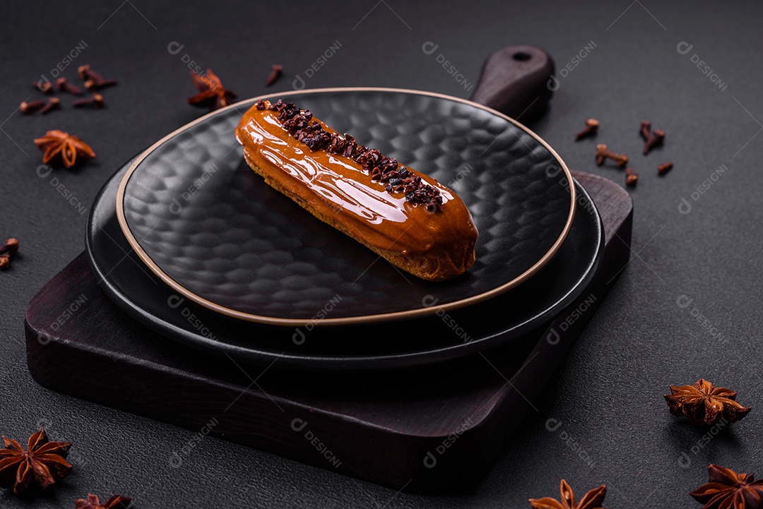 Delicioso eclair fresco com creme de chocolate em uma placa de cerâmica preta sobre um fundo escuro de concreto