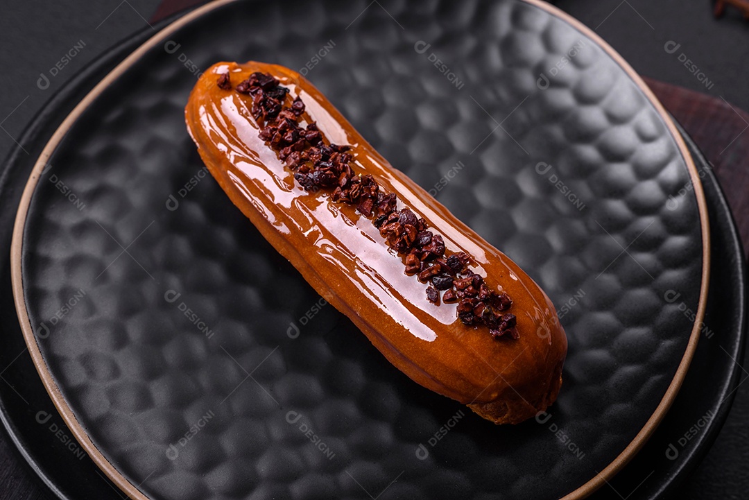 Delicioso eclair fresco com creme de chocolate em uma placa de cerâmica preta sobre um fundo escuro de concreto