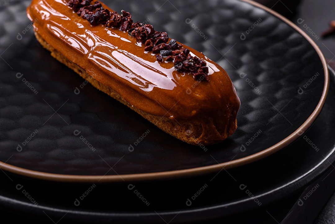 Delicioso eclair fresco com creme de chocolate em uma placa de cerâmica preta sobre um fundo escuro de concreto