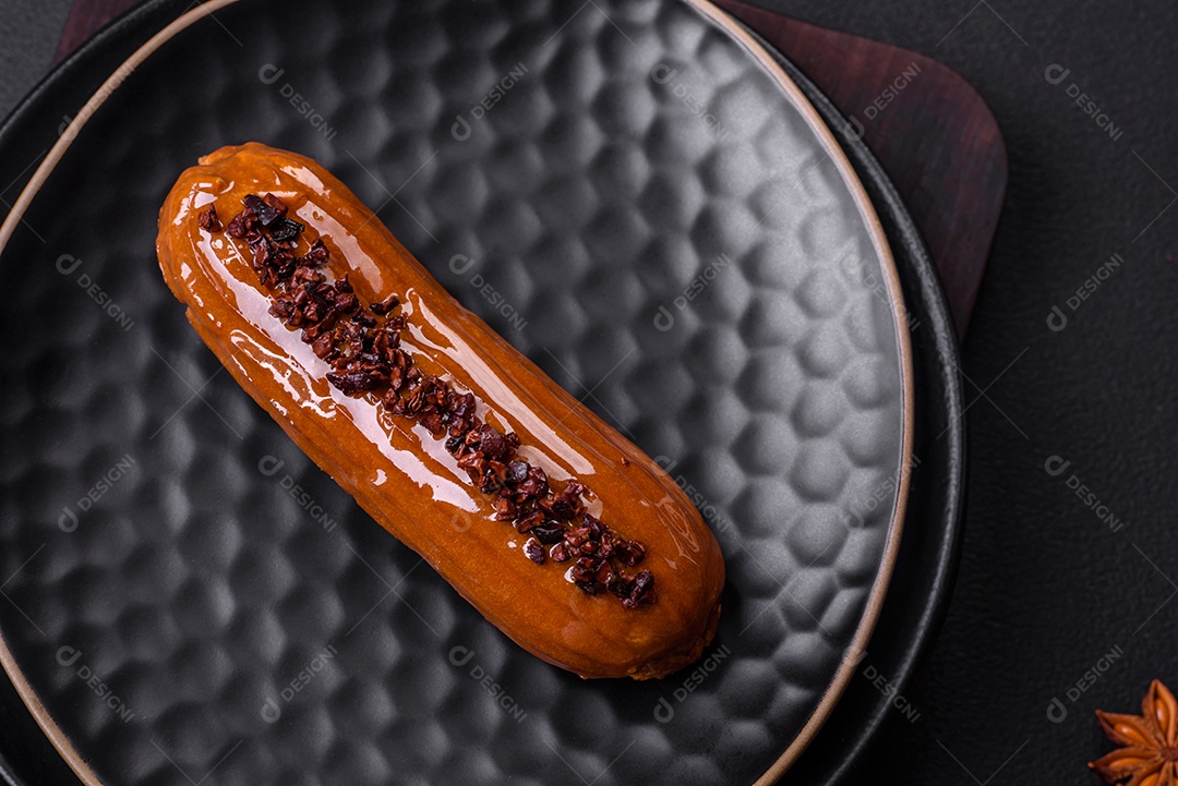 Delicioso eclair fresco com creme de chocolate em uma placa de cerâmica preta sobre um fundo escuro de concreto