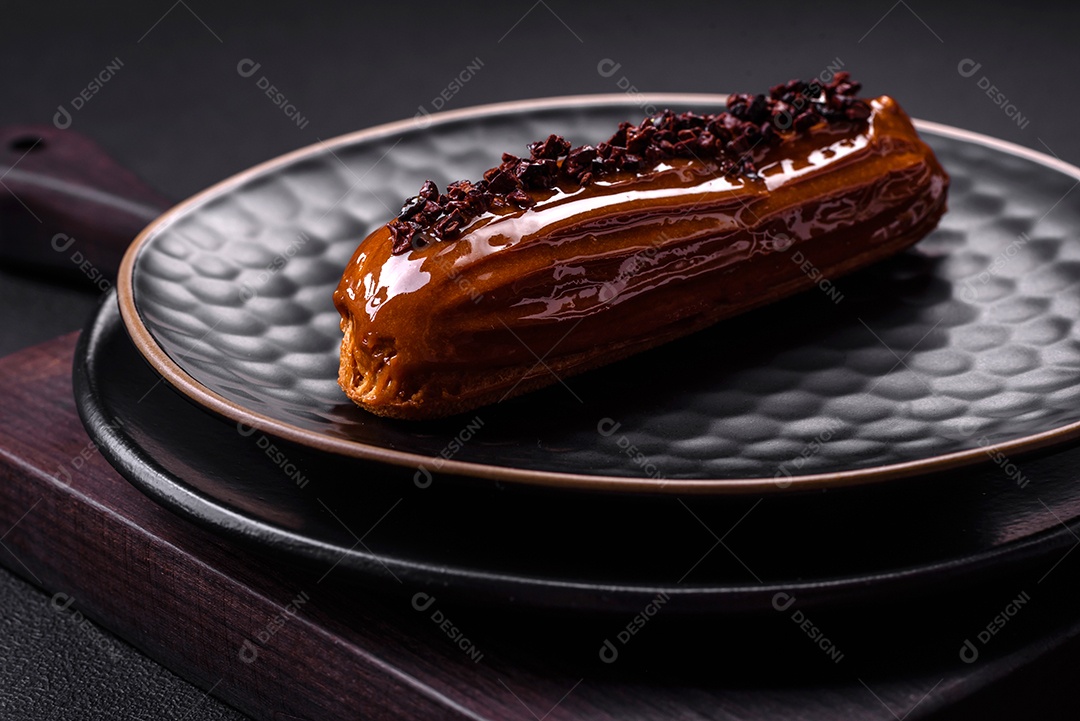 Delicioso eclair fresco com creme de chocolate em uma placa de cerâmica preta sobre um fundo escuro de concreto