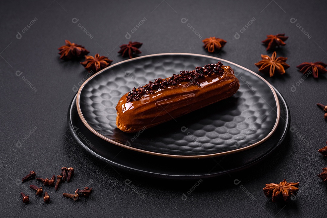 Delicioso eclair fresco com creme de chocolate em uma placa de cerâmica preta sobre um fundo escuro de concreto