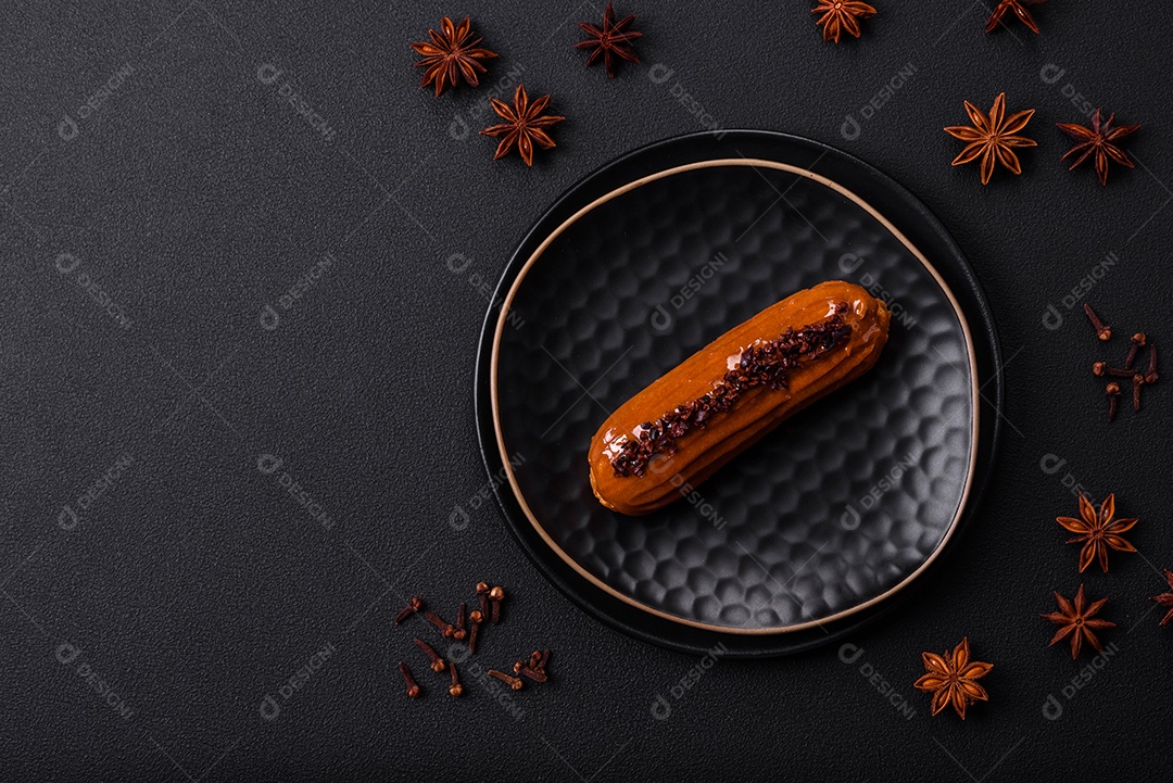 Delicioso eclair fresco com creme de chocolate em uma placa de cerâmica preta sobre um fundo escuro de concreto