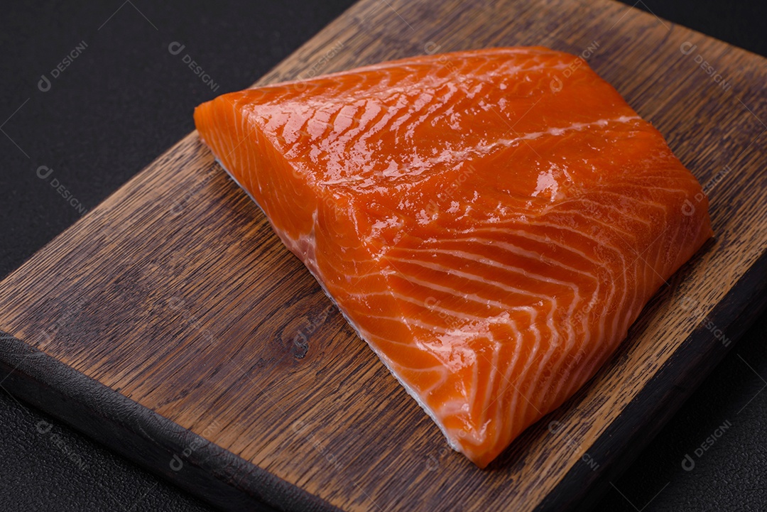 Filé de peixe salmão vermelho cru com sal, especiarias e ervas sobre um fundo escuro de concreto