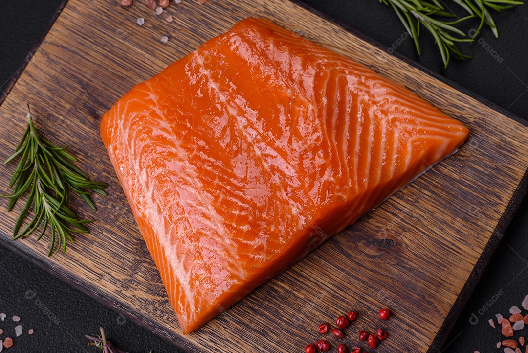 Filé de peixe salmão vermelho cru com sal, especiarias e ervas sobre um fundo escuro de concreto
