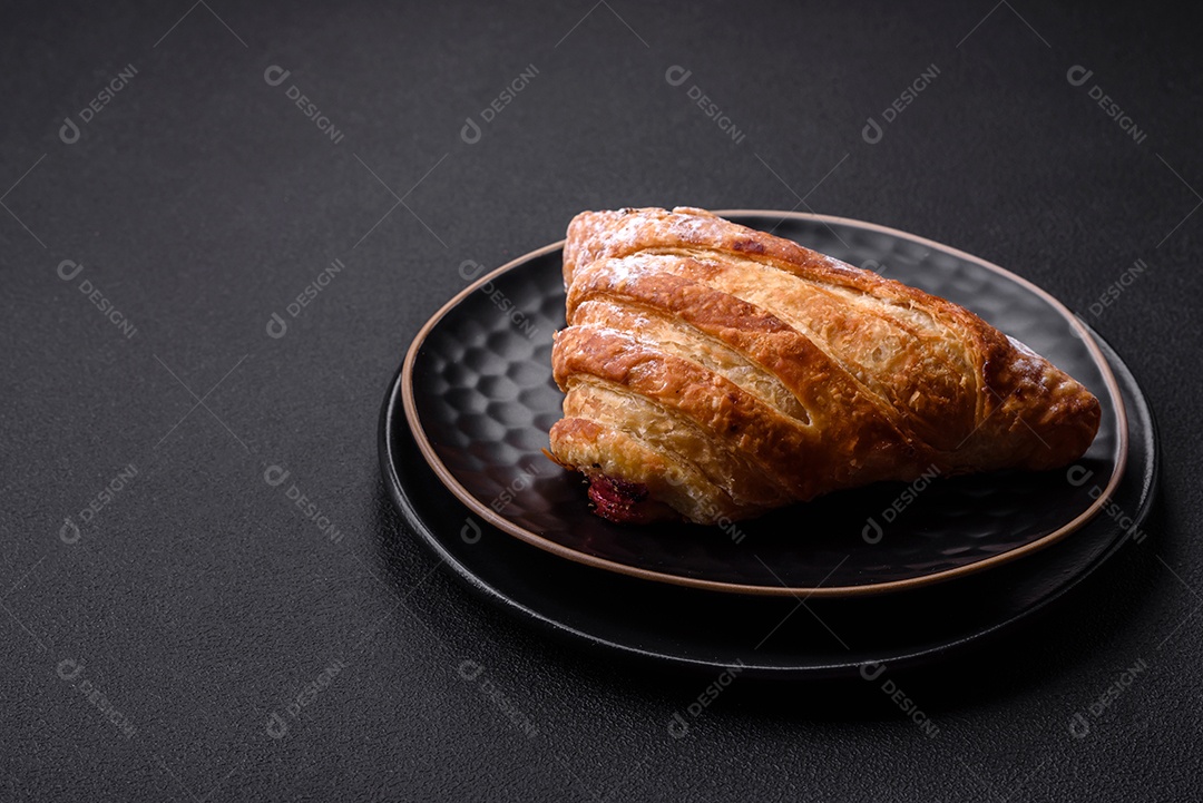 Delicioso pão crocante fresco com geléia em uma placa de cerâmica preta sobre um fundo escuro de concreto
