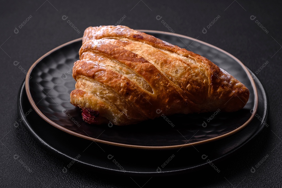 Delicioso pão crocante fresco com geléia em uma placa de cerâmica preta sobre um fundo escuro de concreto