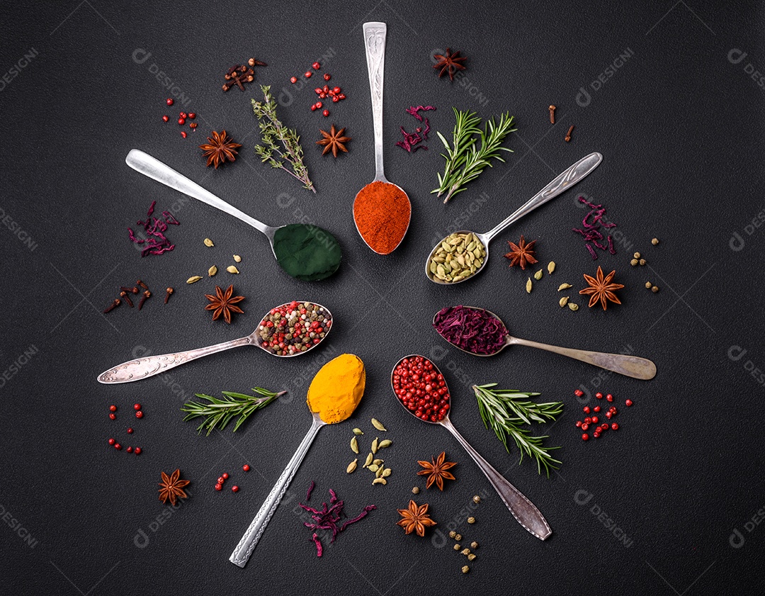 Variação de especiarias em colheres de metal páprica, açafrão, cardamomo, uma mistura de pimenta da Jamaica, tomilho, alecrim e sal sobre um fundo escuro de concreto