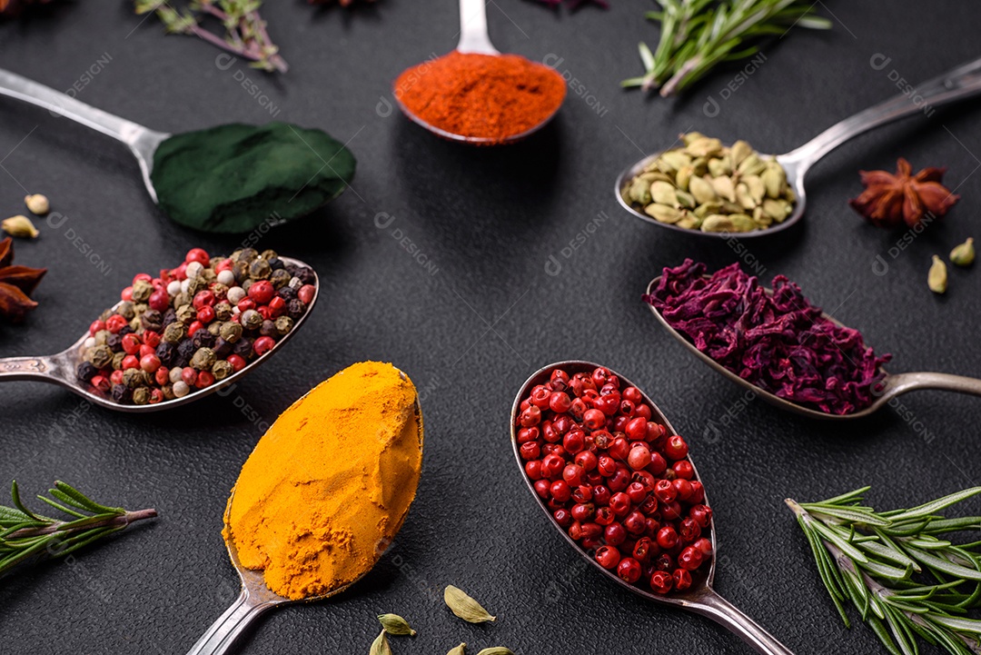 Variação de especiarias em colheres de metal páprica, açafrão, cardamomo, uma mistura de pimenta da Jamaica, tomilho, alecrim e sal sobre um fundo escuro de concreto