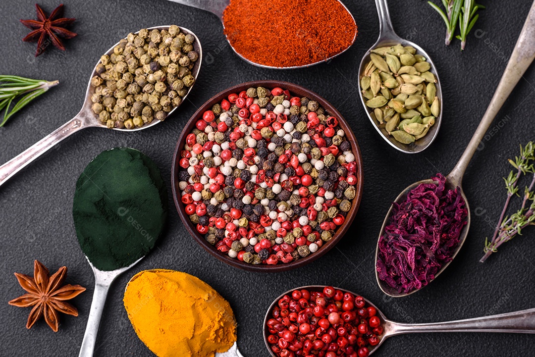 Variação de especiarias em colheres de metal páprica, açafrão, cardamomo, uma mistura de pimenta da Jamaica, tomilho, alecrim e sal sobre um fundo escuro de concreto