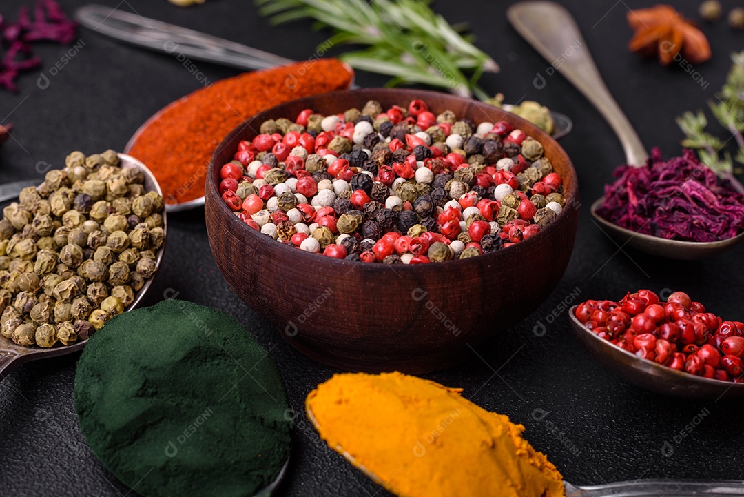 Variação de especiarias em colheres de metal páprica, açafrão, cardamomo, uma mistura de pimenta da Jamaica, tomilho, alecrim e sal sobre um fundo escuro de concreto