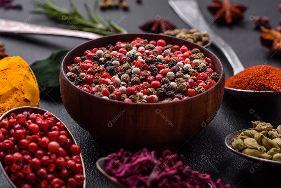 Variação de especiarias em colheres de metal páprica, açafrão, cardamomo, uma mistura de pimenta da Jamaica, tomilho, alecrim e sal sobre um fundo escuro de concreto