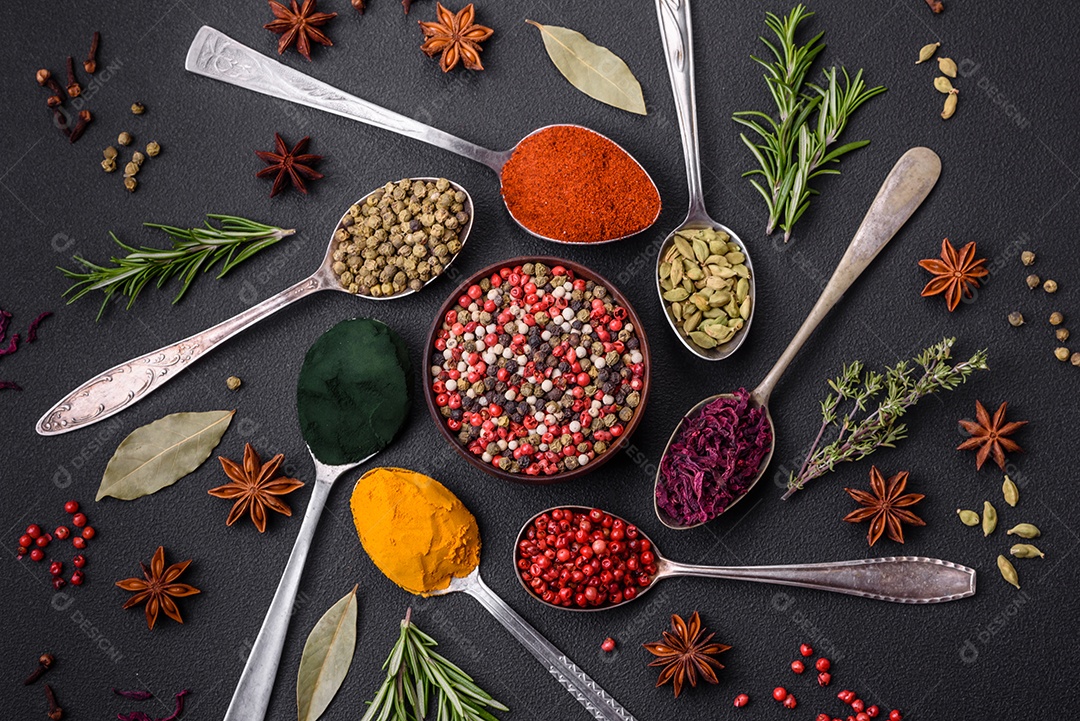 Variação de especiarias em colheres de metal páprica, açafrão, cardamomo, uma mistura de pimenta da Jamaica, tomilho, alecrim e sal sobre um fundo escuro de concreto