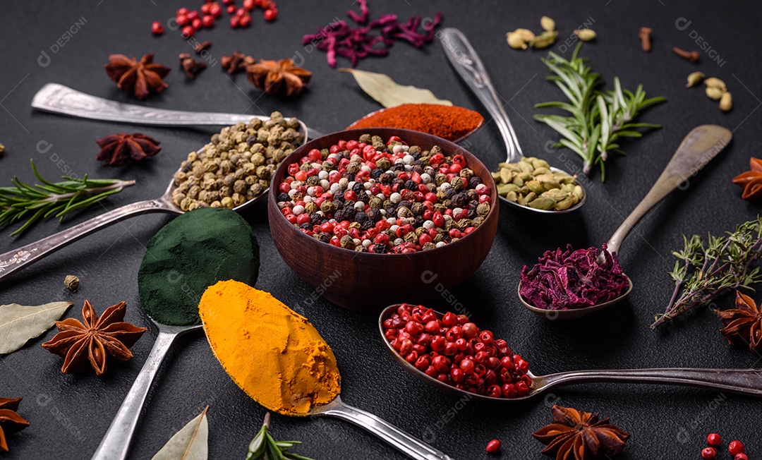 Variação de especiarias em colheres de metal páprica, açafrão, cardamomo, uma mistura de pimenta da Jamaica, tomilho, alecrim e sal sobre um fundo escuro de concreto