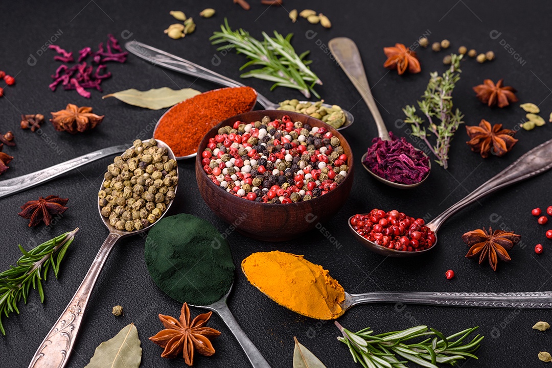 Variação de especiarias em colheres de metal páprica, açafrão, cardamomo, uma mistura de pimenta da Jamaica, tomilho, alecrim e sal sobre um fundo escuro de concreto