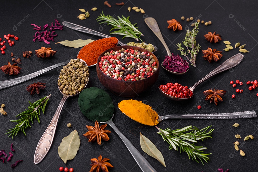 Variação de especiarias em colheres de metal páprica, açafrão, cardamomo, uma mistura de pimenta da Jamaica, tomilho, alecrim e sal sobre um fundo escuro de concreto