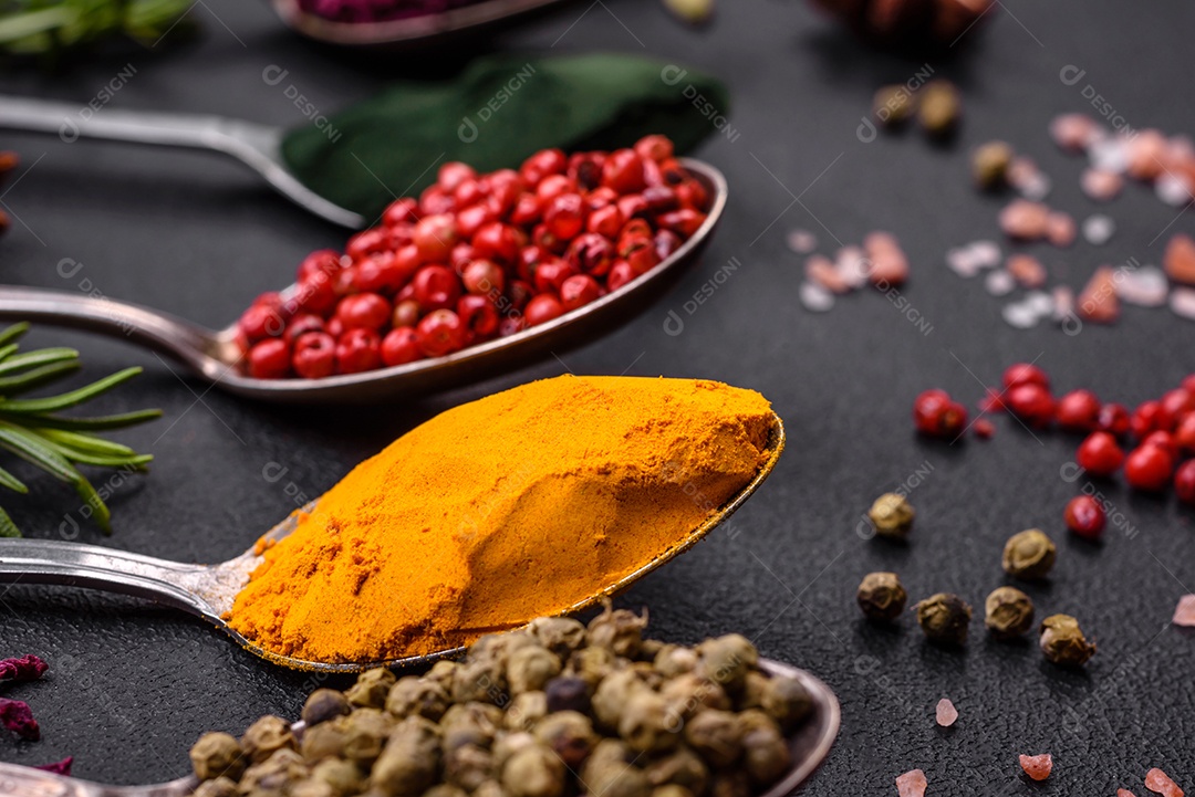 Variação de especiarias em colheres de metal páprica, açafrão, cardamomo, uma mistura de pimenta da Jamaica, tomilho, alecrim e sal sobre um fundo escuro de concreto