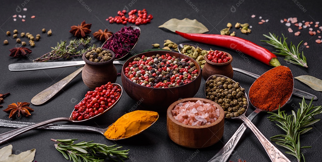 Variação de especiarias em colheres de metal páprica, açafrão, cardamomo, uma mistura de pimenta da Jamaica, tomilho, alecrim e sal sobre um fundo escuro de concreto