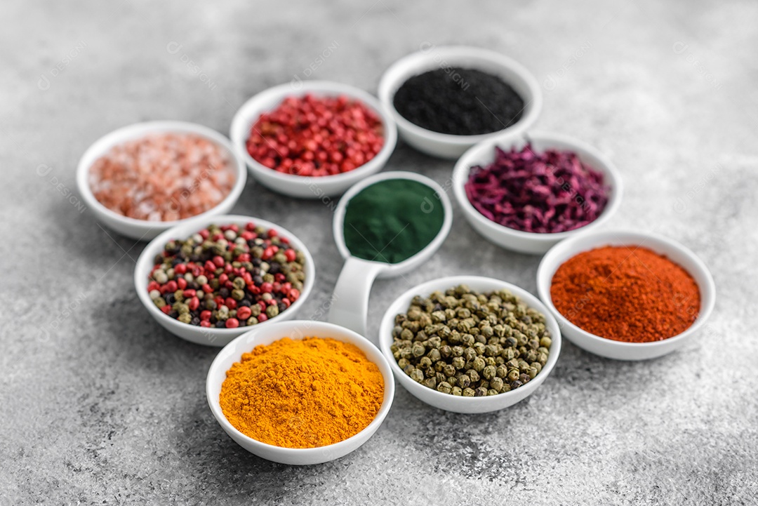 Variação de especiarias em colheres de metal páprica, açafrão, cardamomo, uma mistura de pimenta da Jamaica, tomilho, alecrim e sal sobre um fundo escuro de concreto