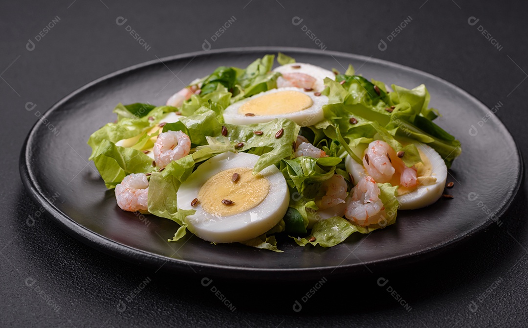 Deliciosa salada fresca e saudável com camarão, ovo, alface e sementes de linho em uma placa de cerâmica preta sobre um fundo de concreto