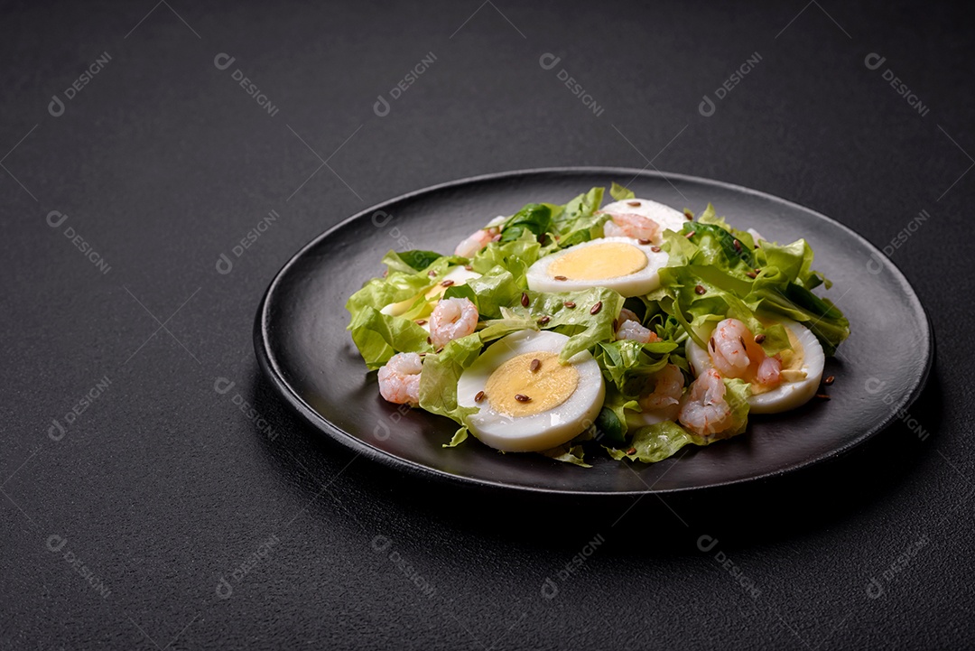 Deliciosa salada fresca e saudável com camarão, ovo, alface e sementes de linho em uma placa de cerâmica preta sobre um fundo de concreto