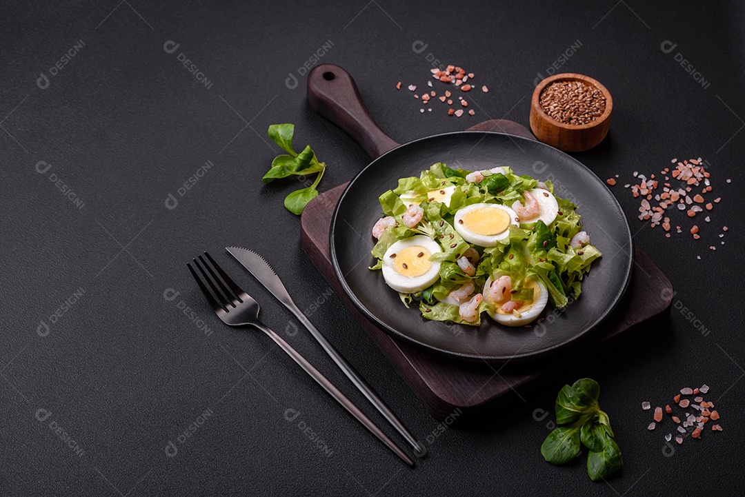 Deliciosa salada fresca e saudável com camarão, ovo, alface e sementes de linho em uma placa de cerâmica preta sobre um fundo de concreto