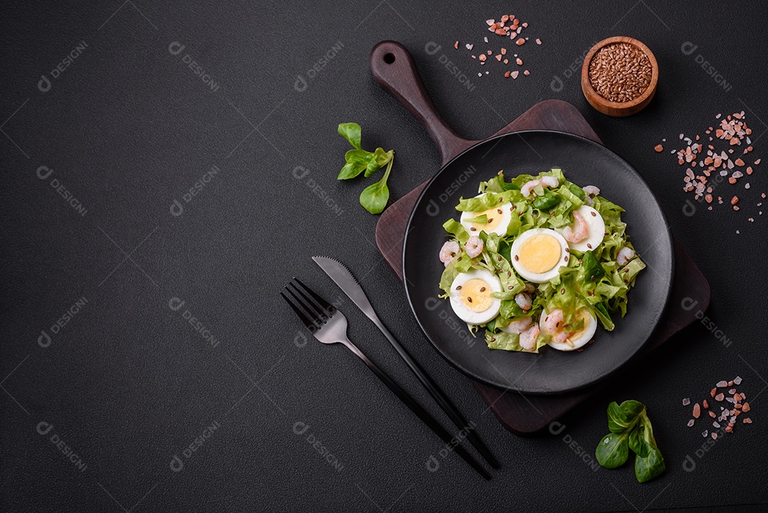 Deliciosa salada fresca e saudável com camarão, ovo, alface e sementes de linho em uma placa de cerâmica preta sobre um fundo de concreto