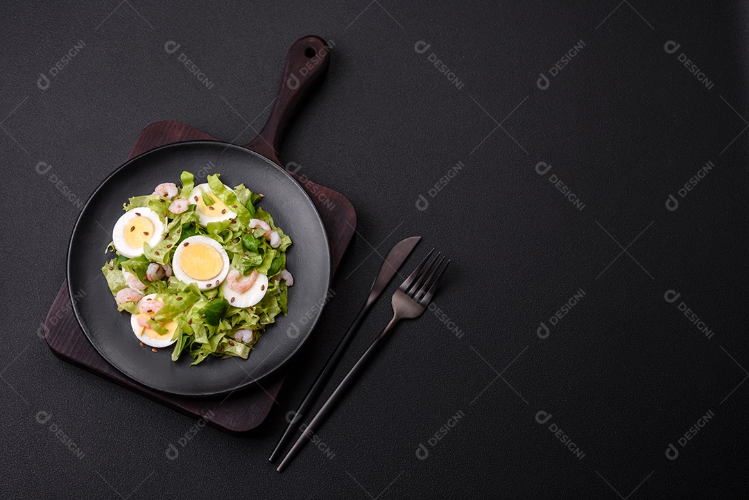 Deliciosa salada fresca e saudável com camarão, ovo, alface e sementes de linho em uma placa de cerâmica preta sobre um fundo de concreto